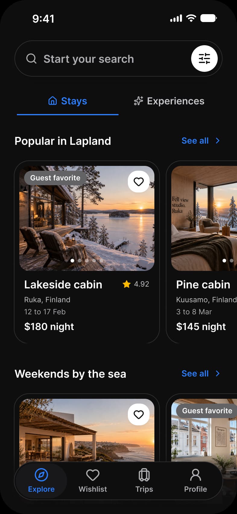 Booking app Explore screen in dark mode: a Start your search capsule with a filter button, Stays and Experiences tabs, Popular in Lapland and Weekends by the sea rows of cabin cards with a favorite heart, rating and price per night, and a floating tab bar